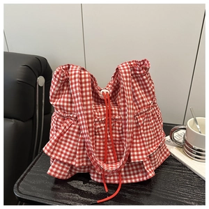 Detail of red gingham tote bag with ruffled edges and drawstring closure on a desk