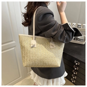 Dettaglio di una borsa tote in paglia con spalline in pelle beige annodate su una modella