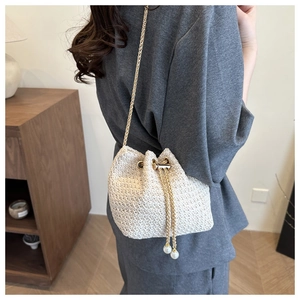 Detail of woven straw bucket bag with gold chain strap and pearl drawstring tassels