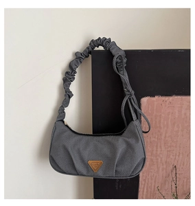 Close-up of gray denim shoulder bag featuring pleated strap and gold triangle plaque