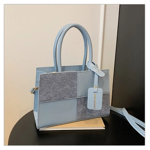 Detail of light blue handbag featuring contrast wool felt panels and fashion tag