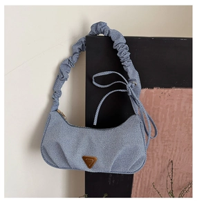 Detail of blue denim fabric texture and vintage metal logo on pleated shoulder bag