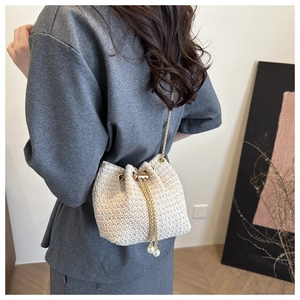 Detail of cream woven bucket bag with pearl drawstring and golden chain strap