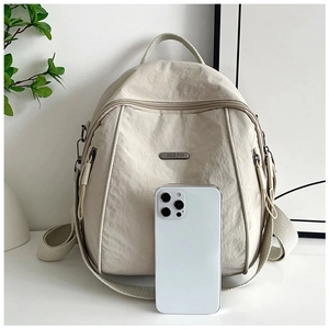 Close-up of beige nylon backpack with brand plaque next to phone for size reference