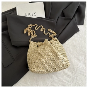 Detail of woven straw bucket bag with gold chain strap on a dark blazer background