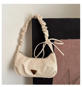 Detailed view of cream hobo bag with ruched strap, bow detail, and triangle plaque