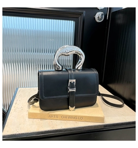 Detail of black crossbody bag with silver curved metal handle on marble surface