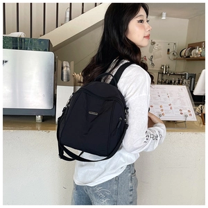 Detail of a minimalist black nylon backpack featuring functional metal logo and side zipper