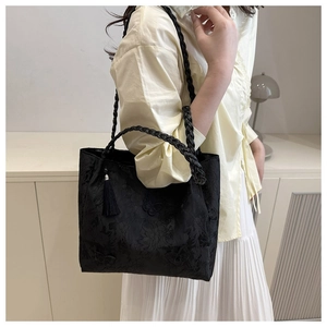 Détail du sac cabas noir avec broderie florale, pompon et bandoulières en tissu tressé