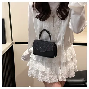 Detail view of black crossbody bag with purple glitter flap and wavy edge on a white dress
