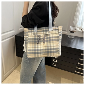 Detail of plaid tote bag with blue handles and woven pendants on a model