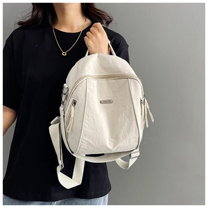 Detail view of cream nylon backpack featuring multiple zip pockets and metal brand plate