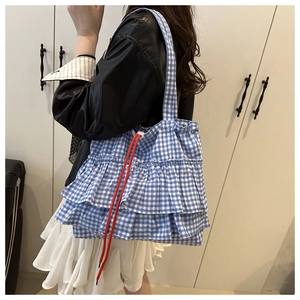 Detail of blue and white checkered tote bag with tiered ruffles and red drawstring accent