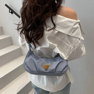 Blue denim crescent hobo bag with a golden triangle emblem shown on a model