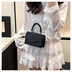 Detail of black crossbody bag featuring a sparkling sequin flap and sleek silver chain strap