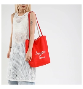Detailed shot of a red canvas tote bag with white beyou and merci text on model