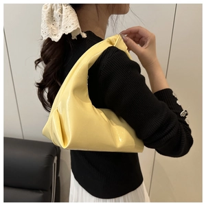 Detail of yellow glossy patent leather baguette bag with knot handle worn by a model