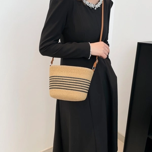 Summer straw bucket bag with black stripes and brown leather strap worn by a model