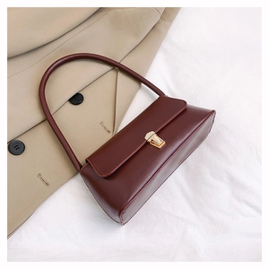 Détail du sac sous le bras en cuir bordeaux avec boucle dorée sur un trench-coat