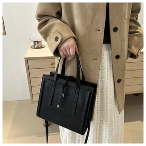 Close-up of minimalist black leather briefcase with metal buckle and detachable shoulder strap