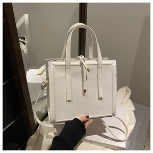 Close-up of white leather handbag featuring golden metal hardware and a top handle