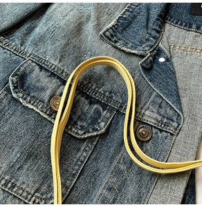 Close-up of blue denim jacket pocket with cargo metal button and yellow crossbody strap