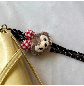 Detail of plush bear bag charm with red bow hanging on a textured leather handbag