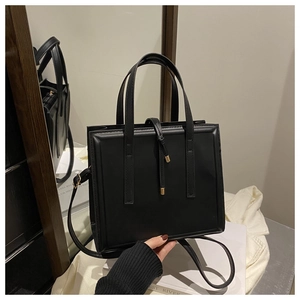 Detail of a minimalist black tote bag with gold-tipped drawstring and crossbody strap