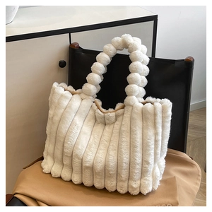 Detail of white plush tote bag with vertical stripes and fluffy pom-pom handle on a chair