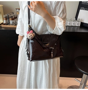 Detail of dark brown glossy shoulder bag with metal eyelets and bear charm