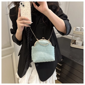 Detalle de bolso concha azul claro en tela texturizada con cierre y asa dorada