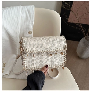 Detail of straw shoulder bag with shell charms and a sleek faux leather strap