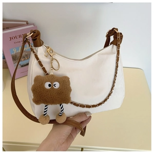 Détail d'un sac blanc avec bandoulière marron, chaîne dorée et charm peluche monstre