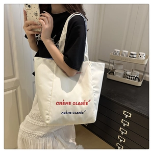 Detail of white canvas tote bag featuring Crème Glacée red and blue embroidered letters
