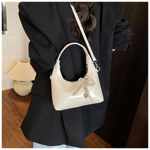 Chic cream leather shoulder bag with pearl bow detail styled on a professional outfit