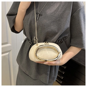 Detail of a creamy patent leather crossbody bag with a large polished golden C-buckle