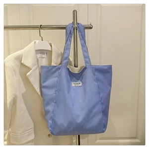 Detail of blue and white striped canvas tote bag with embroidered fashion text label