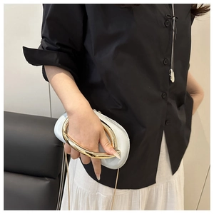 Detail of elegant oval clutch with gold U-shaped handle and slim metal chain strap