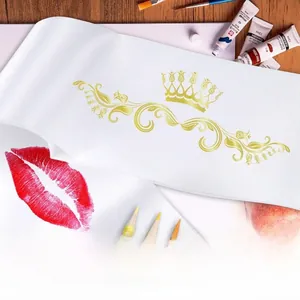 Detail of white satin sash with gold crown and red lip prints on wooden surface