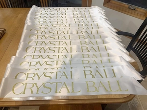 Batch view of white satin sashes with gold glitter Crystal Ball lettering for party events