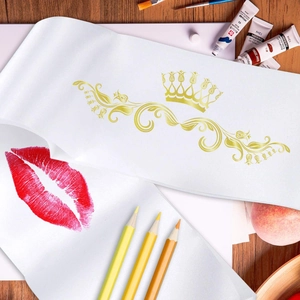 White satin sash with gold crown pattern and red lip print on a wooden desk background