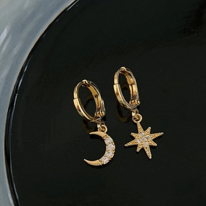 Gold asymmetrical earrings with rhinestone star and moon charms on black background