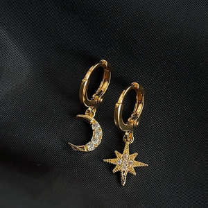 Gold star and moon asymmetric earrings with clear cubic zirconia on black fabric