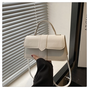 Detailansicht der cremefarbenen Baguette-Tasche aus Leder mit Griff im sanften Licht