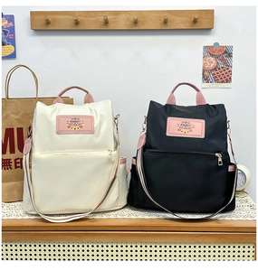 Detail of vintage style nylon backpacks in cream and black with pink contrast handles