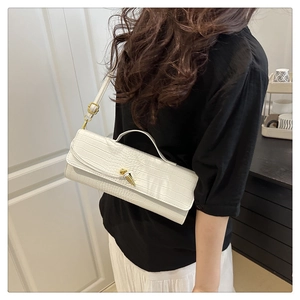 Detail showing white croc-embossed baguette bag with gold knot lock on a model shoulder