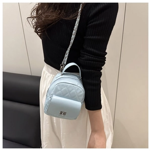 Close-up of light blue mini backpack with quilted pattern and silver chain strap on model