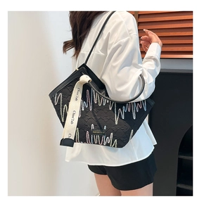 Détail de la broderie ondulée colorée et de la sangle à logo sur un sac fourre-tout noir