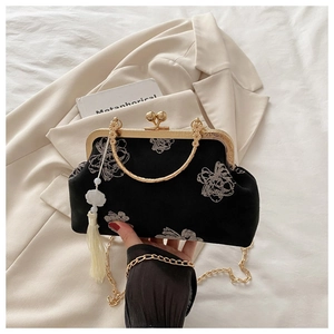 Detail of a black floral velvet bag with gold clasp and white flower tassel pendant