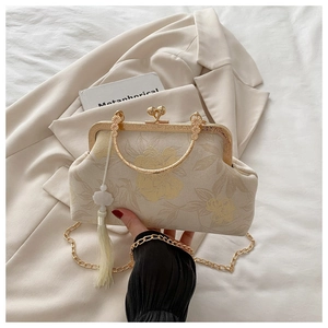 Detail view of cream fabric floral kiss-lock clutch bag with golden handle and tassel